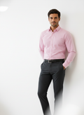 Man wearing a pink dress shirt and black pants against a white background
